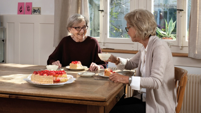 Zwei Seniorinnen bei Kaffee und Kuchen am Küchentisch