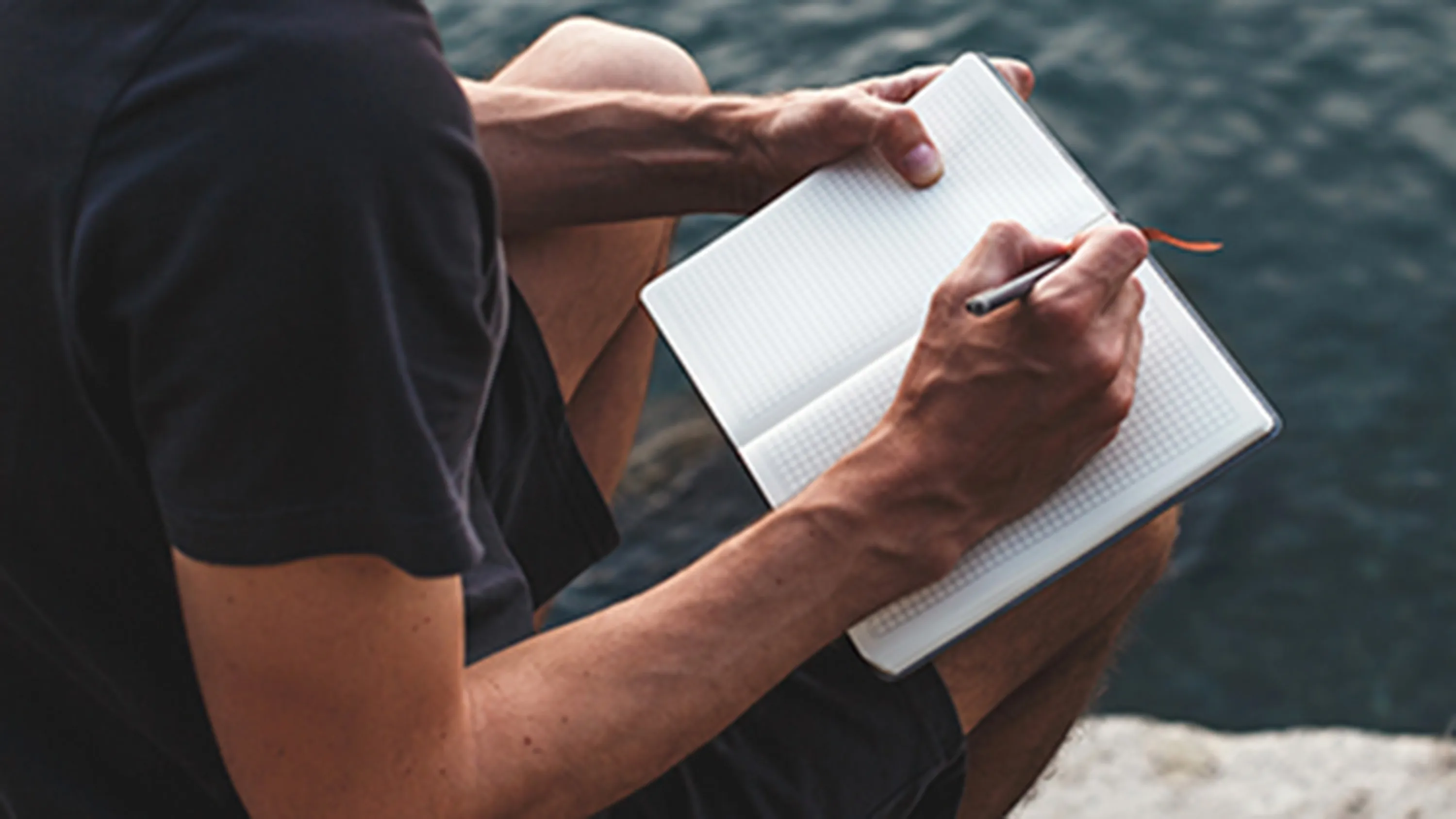 Un signore scrive su un taccuino e guarda il lago.