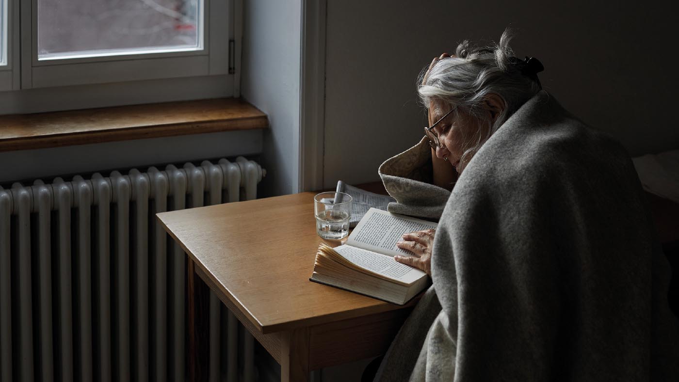 Donna anziana seduta a un tavolo che legge un libro.